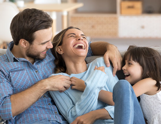 Padre e hija haciendo cosquillas a la madre mientras se ríen sentados en el sofá