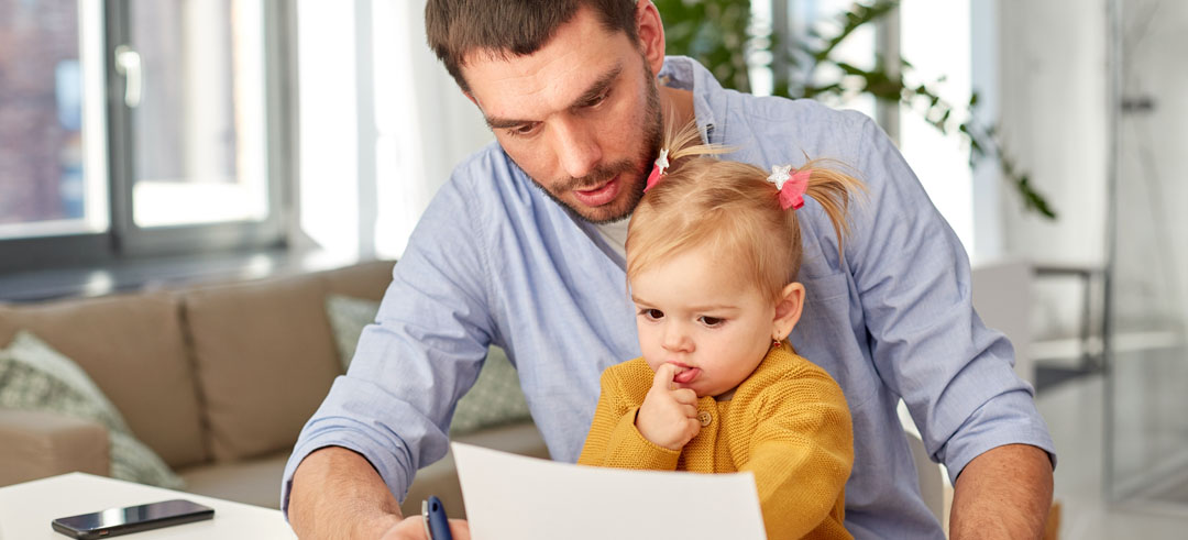 Hombre visualizando un documento mientras sostiene a su hija pequeña